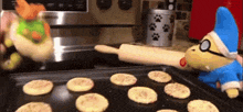 a stuffed animal is standing next to a tray of cookies on a stove .