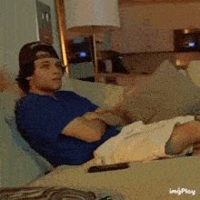 a man is laying on a couch with his arms crossed and a remote control in front of him