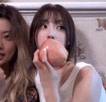 two women are sitting next to each other one is eating an apple .