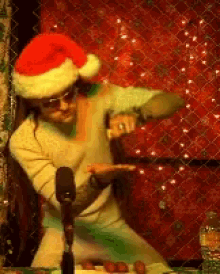 a man wearing a santa hat and sunglasses is dancing in front of a microphone