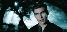 a man with blue eyes is standing under a tree in the dark .