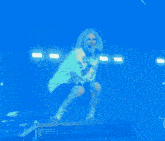 a woman in a yellow hoodie is singing into a microphone while squatting on a stage