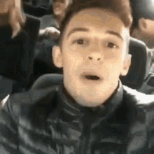 a young man in a black jacket is sitting on a bus making a funny face .