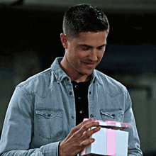 a man in a denim shirt is holding a gift with a pink ribbon
