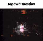 a woman in a pink dress singing into a microphone on a stage with the words togawa tuesday above her