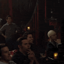 a group of men are sitting in a dark room with candles in the background