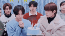 a group of young men are standing around a cake with candles on it .