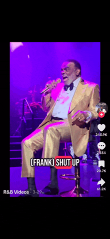 a man in a gold suit is singing into a microphone while sitting on a chair .