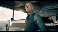 a bald man in a suit and tie stands in a room