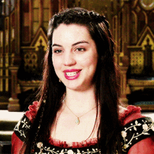 a woman wearing a necklace and a red dress smiles for the camera