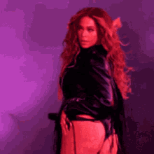 a woman with long red hair is standing in front of a purple background and holding her butt .