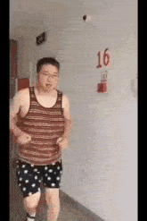 a man in a striped tank top and shorts is running in a hallway .