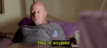 a bald man is laying on a bed with his eyes closed and a purple pillow .