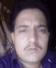 a close up of a man 's face with a mustache and a purple shirt .