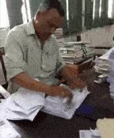 a man in a green shirt sits at a desk with a stack of papers