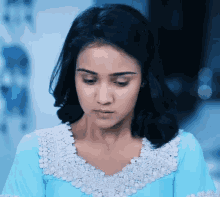 a woman in a blue dress with white lace around her neck looks down