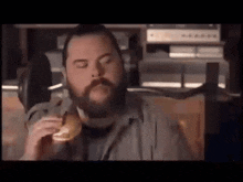 a man with a beard is eating a hamburger with his eyes closed .