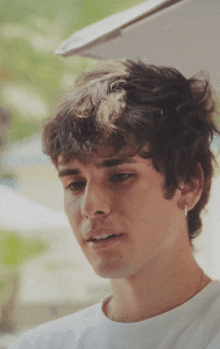 a young man with curly hair is wearing a white t-shirt and earrings