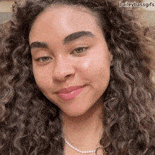 a woman with curly hair and a pearl necklace smiles for the camera