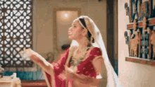 a woman in a red sari and white veil is standing in a room holding something in her hands .