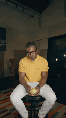 a man wearing glasses and a yellow shirt is holding an apple