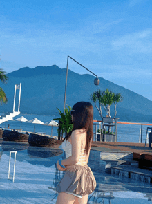 a woman stands in front of a pool with mountains in the background