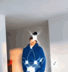 a man wearing a blue adidas hoodie and a beanie is standing in a hallway