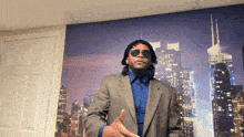 a man in a suit and sunglasses stands in front of a cityscape