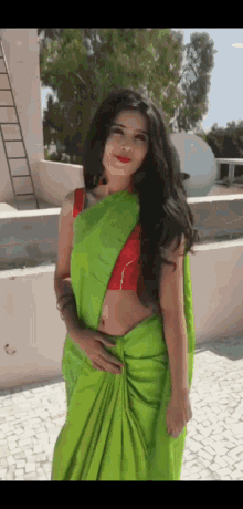 a woman in a green saree with a red blouse is standing on a rooftop .