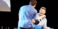 two men are laughing on a stage and one of them is holding another man 's arm