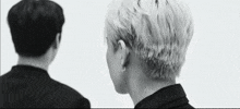 a black and white photo of two men standing next to each other . one of the men has a very short haircut .
