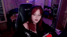 a woman with red hair is sitting in a gaming chair wearing headphones .