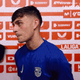 a man wearing a blue laliga shirt stands in front of a wall of advertisements