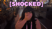 a woman covering her mouth with her hand and the words [ shocked ] behind her