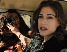 two women are sitting in a car one is taking a picture with a camera