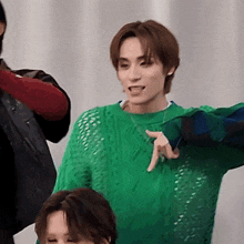 a man wearing a green sweater is pointing at the camera
