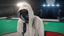 a person wearing a mask and a hoodie is standing in front of a microphone