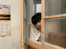 a person looking out a window with a calendar on the wall