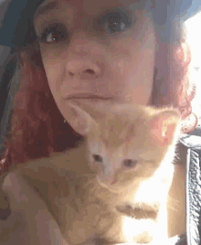 a woman with red hair is holding a cat in her lap