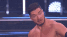 a shirtless man with a beard is standing in a boxing ring on a stage .