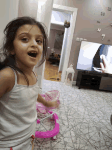 a little girl is playing with a pink walker in front of a clock that has the numbers 7 and 8 on it