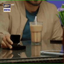a man is sitting at a table holding a box with a ring in it and a cup of coffee with a straw