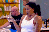 a woman in a white tank top is holding a wine glass in front of a man in a black shirt with @adore written on it