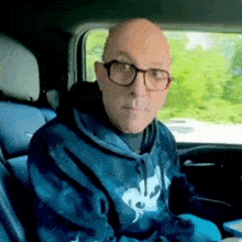 a bald man with glasses is sitting in the back seat of a car .
