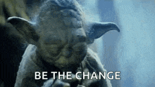 a close up of a statue of yoda with the words `` be the change '' written on it .