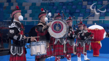 a group of men in kilts are playing drums in front of a sign that says " beijing 2022 "