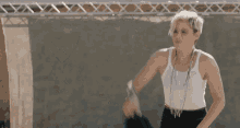a woman in a white tank top is standing in front of a fence .