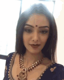 a woman with a red dot on her forehead is wearing a blue top and a gold necklace