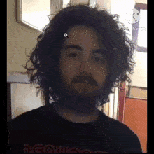 a man with curly hair and a beard is wearing a black shirt and looking at the camera .