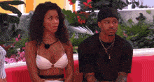 a woman in a bikini sits next to a man on a red couch